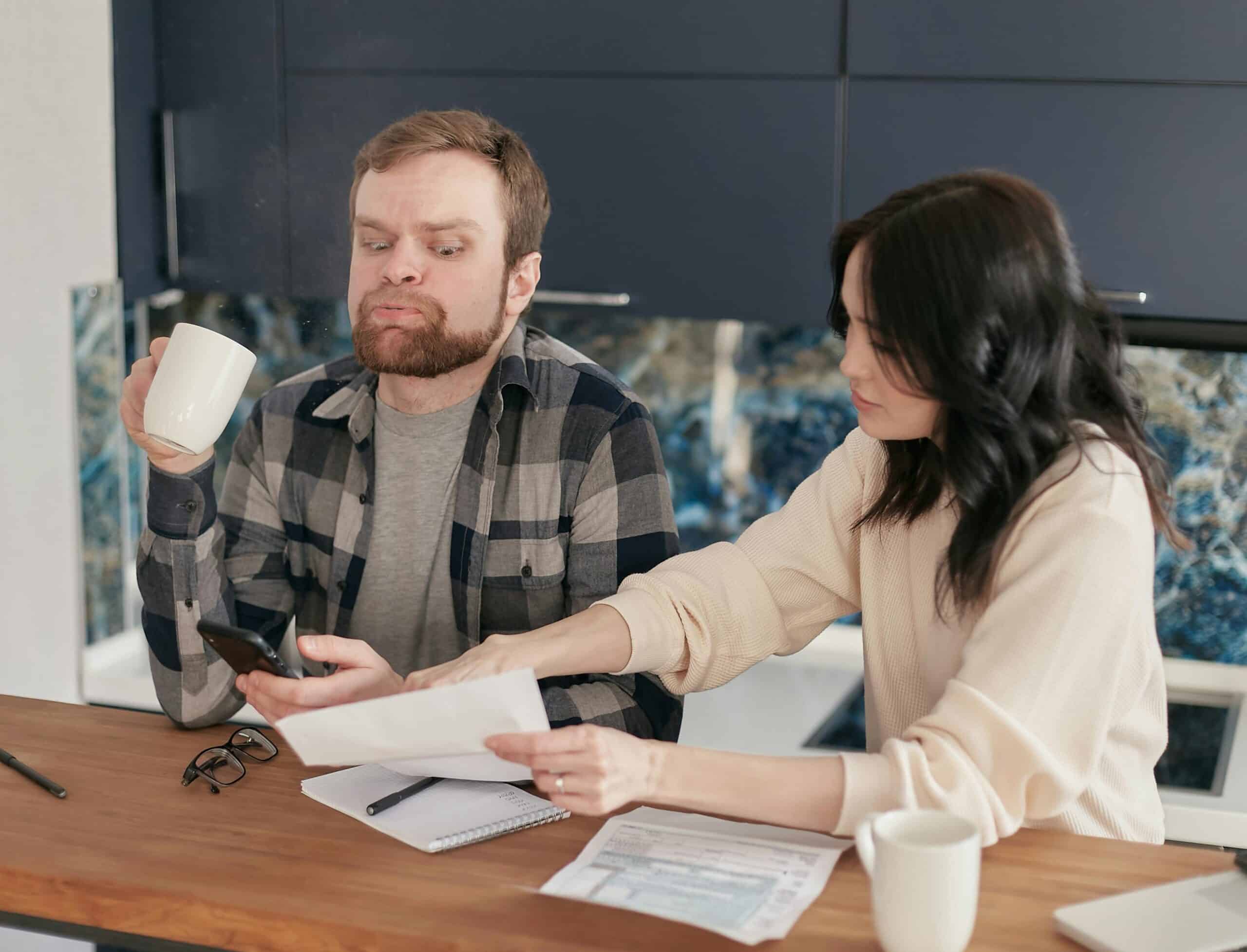 A couple looks worried as they review bills at their kitchen table, reflecting financial concerns.